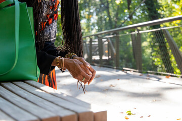 the hands of an African American woman with sister locs in her hair wearing several stone and copper bracelets and a green ring with fallen autumn leaves on the ground at Atlanta Botanical Garden