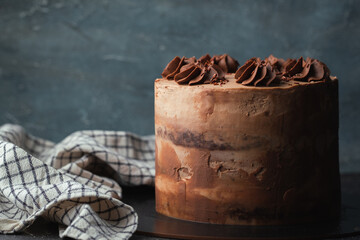 Chocolate sponge cake with brown frosting decorated with chocolate buttercream topping on rustic concrete background