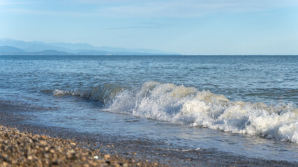 Fototapeta na wymiar Blue sea wave with white foam on a pebble beach