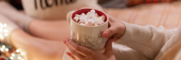 cup of hot chocolate or coffee drink with marshmallows in female holding hands of woman in knitted...