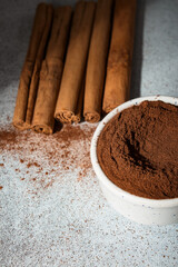 Ceylon cinnamon sticks and ground cinnamon bowl. Carelessly scattered cinnamon on the background.