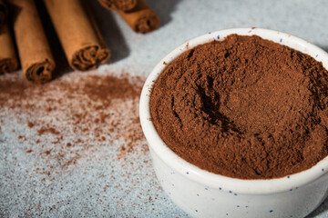 Ceylon cinnamon sticks and ground cinnamon bowl. Carelessly scattered cinnamon on the background.