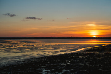 Naklejka premium A beautiful sunset at low tide. The sand has a rippled texture and the water is catching the golden light. The view is from Ramsgate looking towards Sandwich, UK