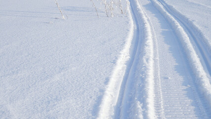 Track of traces from a snowmobile in drifts of white snow. Nature and outdoor. Winter theme wallpaper or background with snowy field