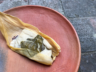One Oaxacan tamale with hoja santa wrapped on the outside of the masa and filled with beans with brick background