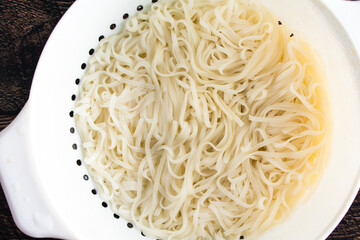 Cooked and Drained Rice Noodles in a White Plastic Colander: Closeup view from above of cooked noodles in a strainer
