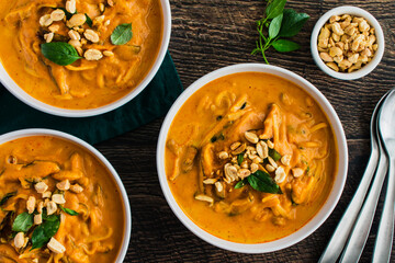 Spicy Thai Curry Pumpkin Noodle Soup Garnished with Peanuts and Thai Basil: Thick soup or stew made with pumpkin, rice noodles, and shiitake mushrooms