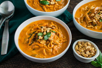 Spicy Thai Curry Pumpkin Noodle Soup Garnished with Peanuts and Thai Basil: Thick soup or stew made with pumpkin, rice noodles, and shiitake mushrooms