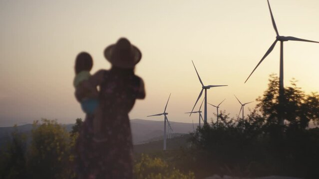 A mother and her daughter are walking near the windmills in the mountains. A woman shows a child how electricity is produced from wind turbines. High quality 4k footage