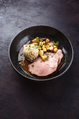 Traditional German pork roast served with bread dumpling and king oyster mushroom in dark beer sauce served as close-up in a Nordic design bowl with copy space