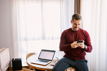 A busy man is responding on client's messages while sitting on the table at home.