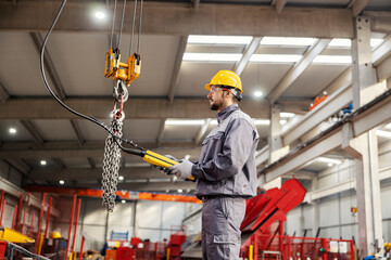 A heavy industry worker relocates chains on hook and commands while standing in a metalwork factory.