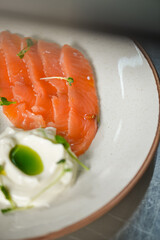 Freshly sliced raw salmon with creamy cheese and herb oil served on a white plate in a modern restaurant kitchen.