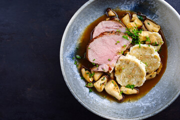 Traditional German pork roast served with bread dumpling and king oyster mushroom in dark beer sauce served as top view in a Nordic design bowl with copy space left