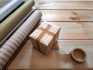 Preparing gifts for Christmas and New Year. DIY packaging. Copy space for text. Top view. Process of wrapping box with surprise in holiday paper. Selective focus. Concept creating festive mood. 