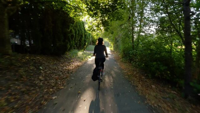 Adventure Woman bike riding on a bicycle trail surrounded by green trees. Summer Sunset. Pitt Meadows, Greater Vancouver, British Columbia, Canada.