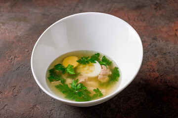 Chicken soup bouillon in a plate on dark stone table