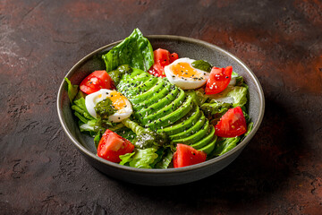 vegetable salad with avocado, poached egg and tomatoes on dark stone table