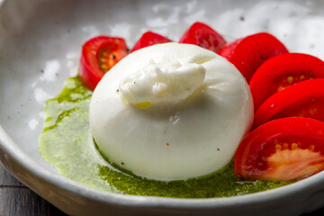 Salad with buratta cheese and tomatoes with pesto sauce on bowl on wooden table macro close up