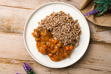 Goulash with beef and carrots with buckwheat on white plate on wooden table top view