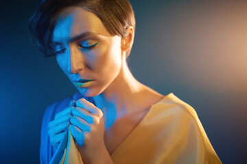 young ukrainian woman in yellow and blue clothes and dress praying for ukraine
