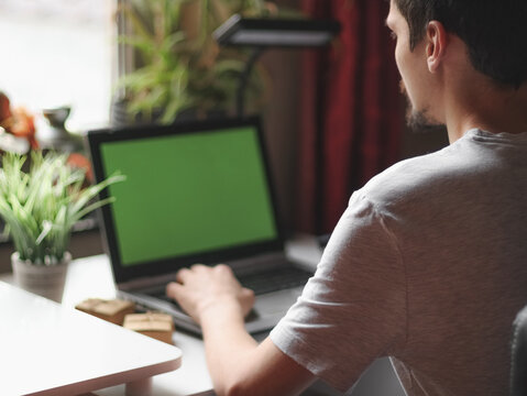 Young caucasian man doing online shopping,sitting in his room with a green screen laptop.