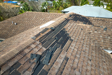 Damaged house roof with missing shingles after hurricane Ian in Florida. Consequences of natural...