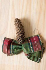 pine cone and bow made from holiday fabric ribbon in green and red plaid on wood