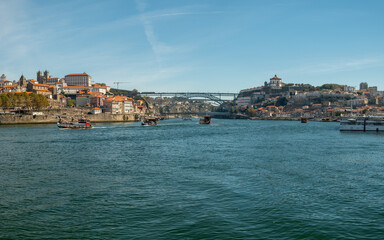 Fototapeta na wymiar Panoramic view over the Douro River and traditional tourist transport boat's and the D. Luis I Bridge in the background. City of Porto in Portugal.