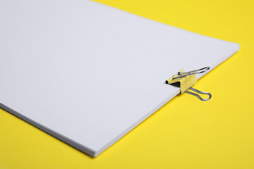 Sheets of paper with clip on yellow background, closeup