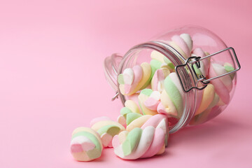 Overturned jar with delicious colorful marshmallows on pink background, space for text