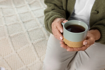 Elderly woman with cup of hot drink indoors, closeup. Home care service