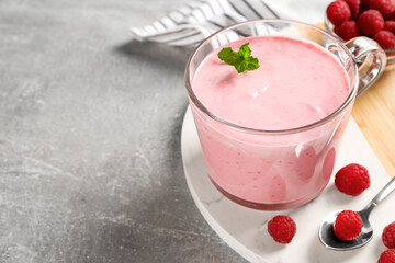 Glass of delicious yogurt with mint and raspberries on grey table, closeup. Space for text