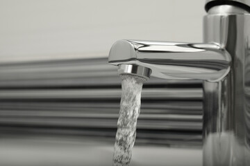 Water flowing from tap on blurred background, closeup. Space for text