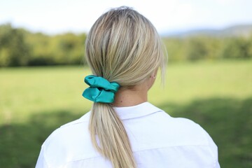 Young blonde woman from behind, wearing a white shirt and scrunchie on her ponytail in a sunny field