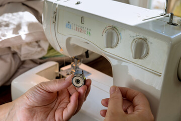 Using sewing machine, seamstress puts threads from metal spools into machine