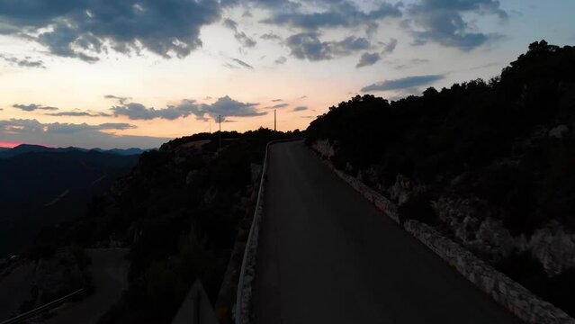 Steigflug mit Drohne auf der Insel Sardinien in Italien am Meer in Europa der K&uuml;ste entlang &uuml;ber eine Berg Stra&szlig;e Bergpass mit Blick auf die Stadt Baunei und mediterraner Landschaft in der D&auml;mmerung 