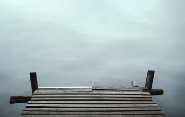 Obraz premium Old wooden pier against the backdrop of the calm water for copy space. Lake shore background.