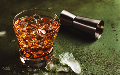Godfather alcoholic cocktail with scotch whiskey, amaretto liqueur and ice. Dark bar counter background, bar tools, copy space