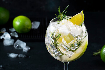 Gin tonic lime alcoholic cocktail drink with dry gin, rosemary, tonic and ice in big wine glass....