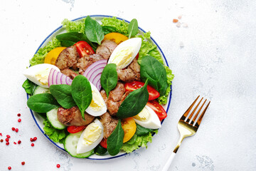 Perigord salad with chicken liver, tomatoes, cucumbers, eggs, lettuce and spinach. Black kitchen table background, top view