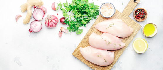 Raw chicken breast fillet, meat on cutting board prepared for cooking with garlic, thyme, spices and pepper. White kitchen table, top view banner