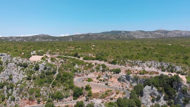 Kurviger Bergweg in Italien auf der Insel Sardinien mit mediterraner Landschaft und Bergen im Hintergrund