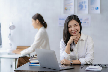 Fototapeta premium Two Asian businesswomen attending two Asian business partners discuss the financial and company planning graph during a budget meeting.