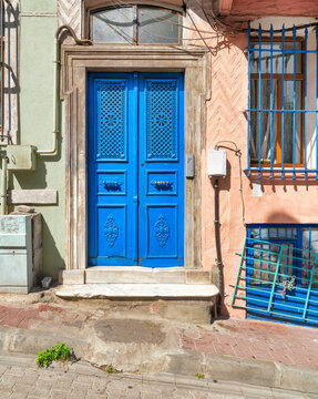 Exterior shot of blue painted decorated metal door beside wrought iron window, in a colorful stone wall painted in orange and green, on city street
