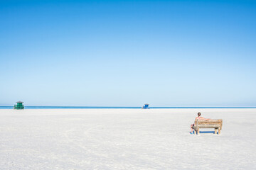 Fototapeta na wymiar A woman is sitting on the bench and looking at the empty beach and ocean