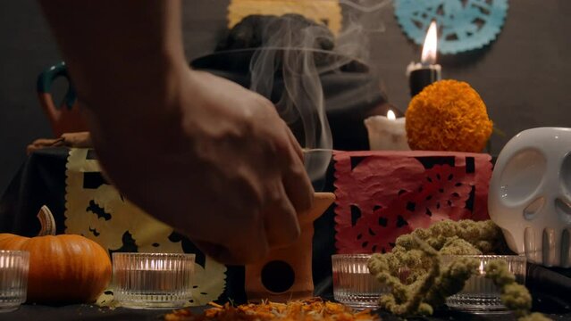 Traditional mexican bread of the dead "pan de muerto" with black ashes in Mexican altar with &ldquo;papel picado&rdquo;, copal, incense burner, cempasuchil flowers, coffee, pumpkin, skull. Slow motion. 