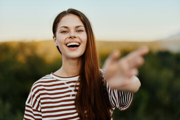 Woman smiling while looking at the camera and pulling her hands to the camera close-up in nature with a view of the mountains. Happy travel lifestyle follow me