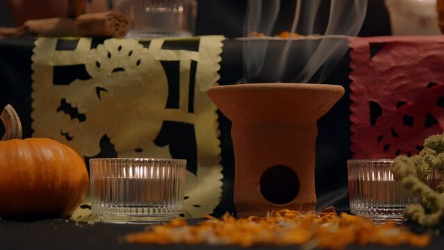 Traditional mexican bread of the dead "pan de muerto" with black ashes in Mexican altar with &ldquo;papel picado&rdquo;, copal, incense burner, cempasuchil flowers, pumpkin. Slow motion, close up, panning