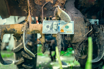 Hundred dollar bill between the teeth of a tractor rototiller close-up. Finance and agricultural...